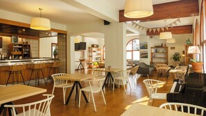 A spacious dining area with wooden tables and chairs, a bar area with stools, and a kitchen visible in the background. - Hotel Medes II (Torroella de Montgrí)