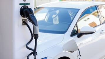 A white car connected to an electric charging station with a visible 'C' logo and indicator lights.