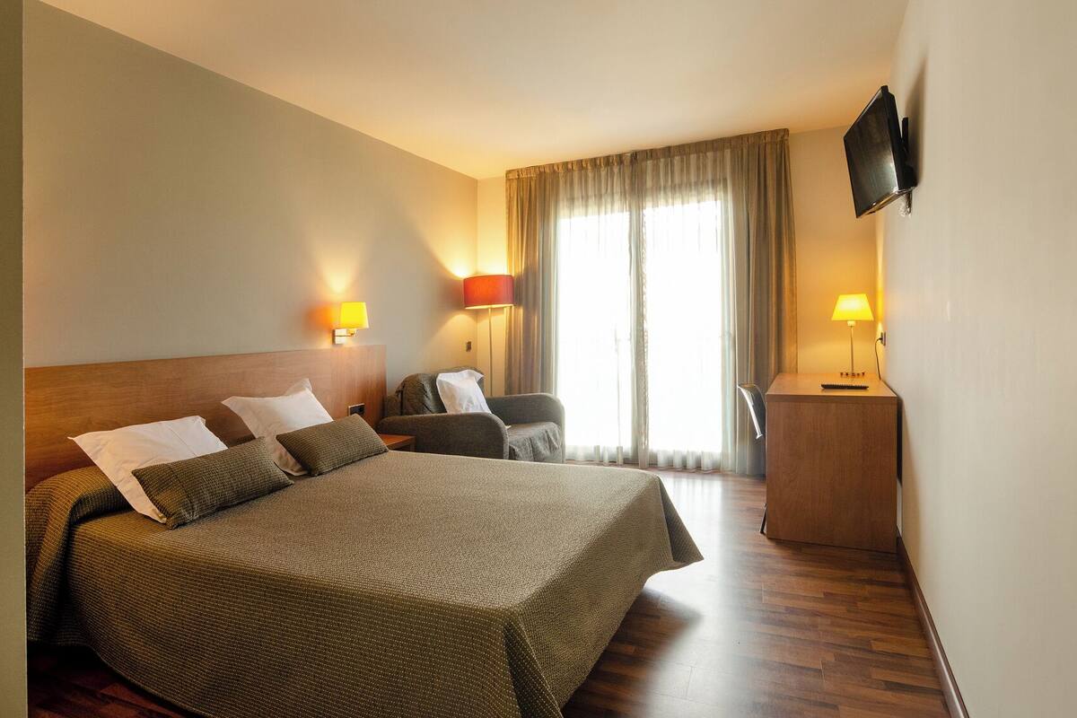 A hotel room with a large bed, two bedside tables, a desk, and a TV mounted on the wall.