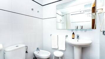 Un baño moderno con azulejos blancos, un bidé, un inodoro, un lavabo y un espejo.