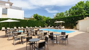 A poolside area with lounge chairs and tables, a swimming pool, and a white building in the background. - Hotel Medes II (Torroella de Montgrí)