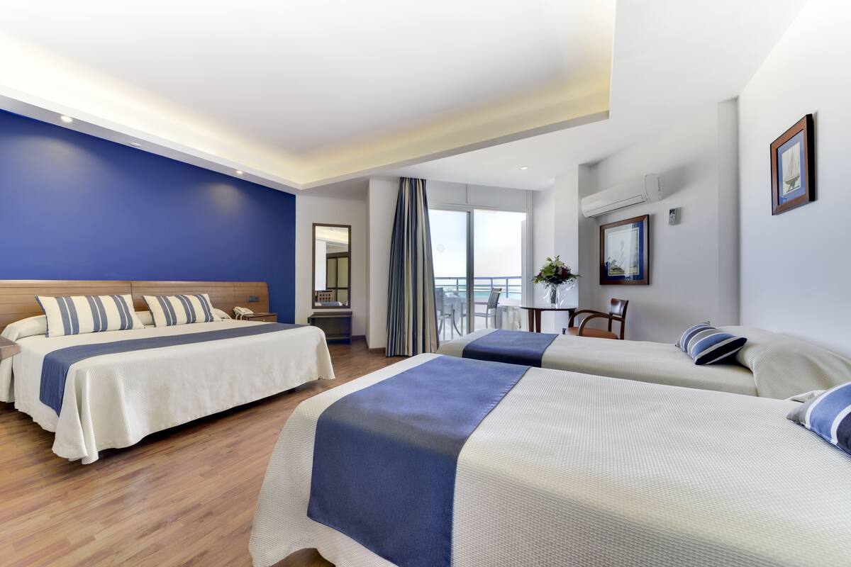 A hotel room with two beds, a balcony, and a view of the sea.