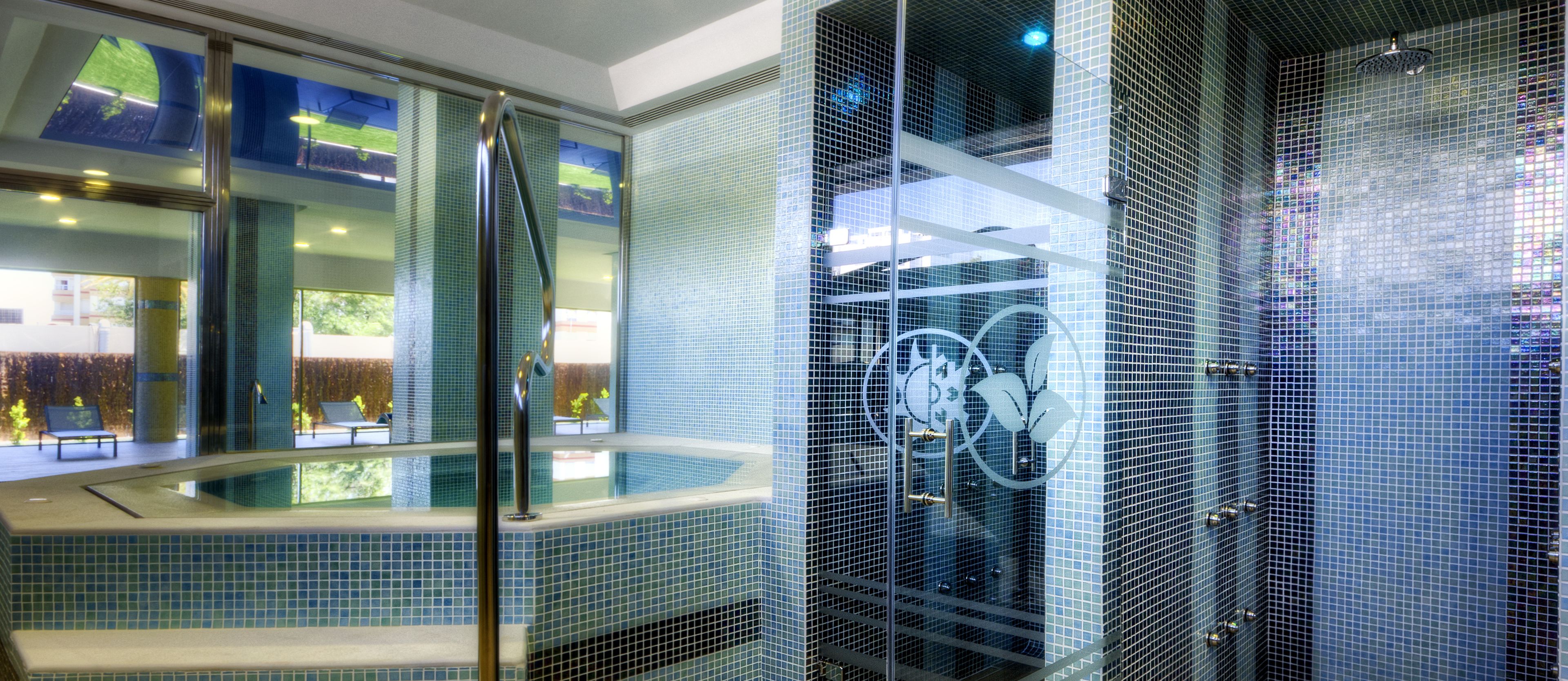 Un baño moderno con un jacuzzi de vidrio, paredes con azulejos y vistas al exterior.