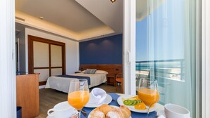 Quarto de hotel com cama, escrivaninha e mesa de café da manhã, com suco de laranja, croissants e uma tigela de frutas.