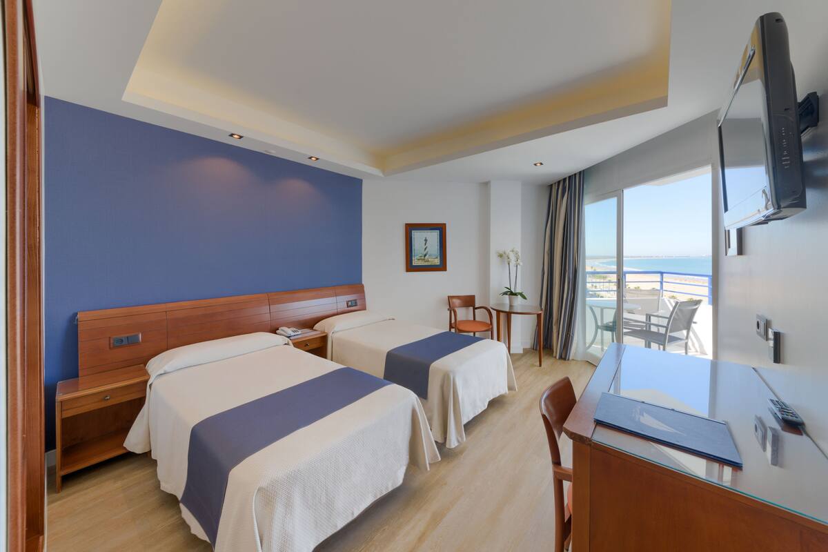 A hotel room with two beds, a desk, a chair, a TV, and a window with a view.