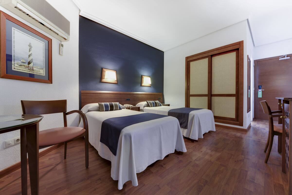 A hotel room with two beds, a desk, a chair, and a wardrobe.