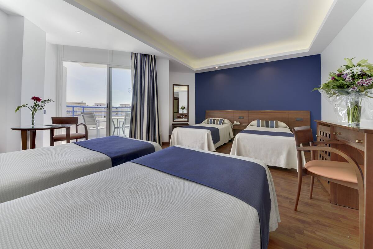 A hotel room with two beds, a balcony, a desk, and a chair.