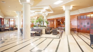 Um hall amplo com pé direito alto, grandes colunas e área de estar central com sofás e poltronas.