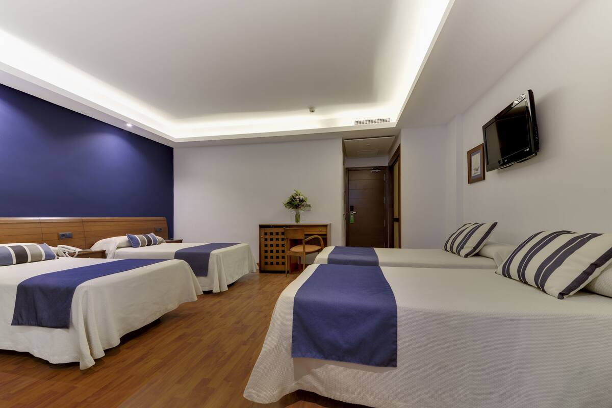A hotel room with two beds, a desk, a chair, a TV, and a door.