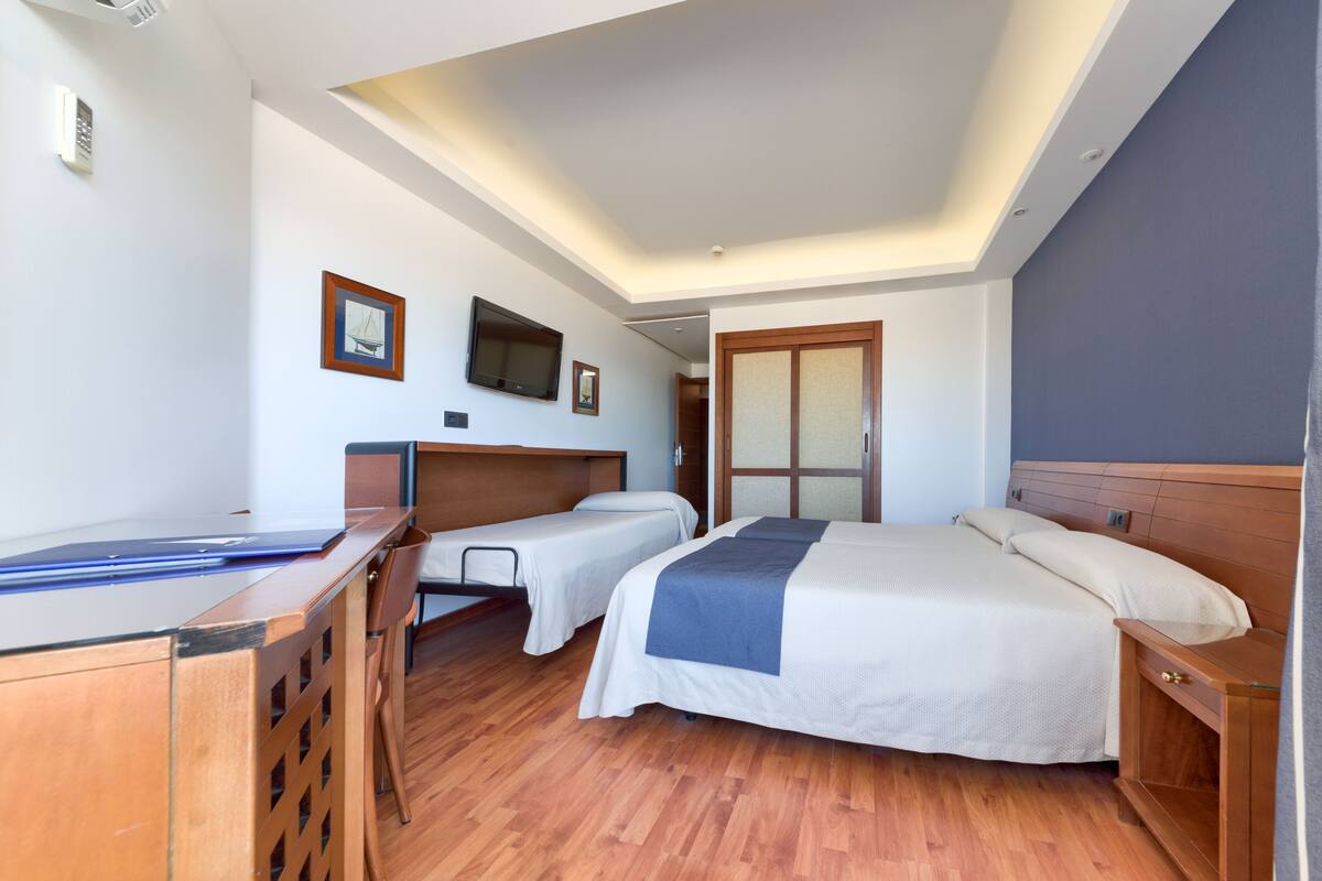 A hotel room with two beds, a desk, a TV, and a wooden floor.
