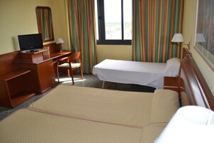 Una habitación de hotel con cama, escritorio, silla, televisión y ventana con cortinas.