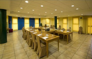 Un salón de conferencias con varias mesas y sillas, equipado con botellas de agua y blocs de notas.