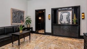 A modern lobby with a black leather sofa, a marble-tiled floor, and framed artwork on the walls. - Hotel Royal (New Orleans)