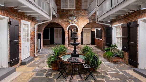 A courtyard with a central fountain, surrounded by potted plants and a stone table. - Hotel Royal (New Orleans)