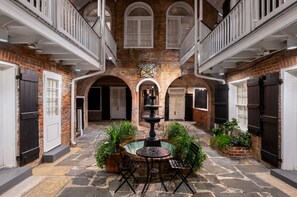 A courtyard with a central fountain, surrounded by potted plants and a stone table. - Hotel Royal (New Orleans)