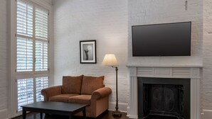 A living room with a brown sofa, a coffee table, a floor lamp, a fireplace, and a TV mounted on the wall. - Hotel Royal (New Orleans)