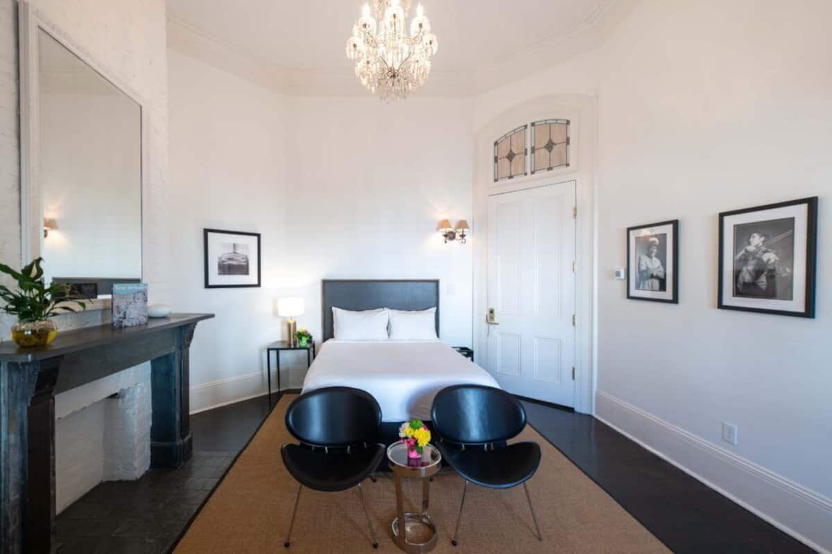 Une chambre d’hôtel avec un grand lit, un lustre, un bureau avec un miroir et deux chaises.