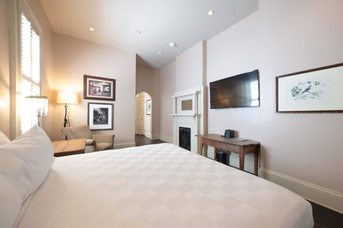 Une chambre d’hôtel avec un grand lit, un bureau, une chaise, une cheminée et des tableaux encadrés aux murs.