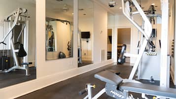 Un gimnasio con diversos equipos de ejercicio, espejos y una televisión en la pared.