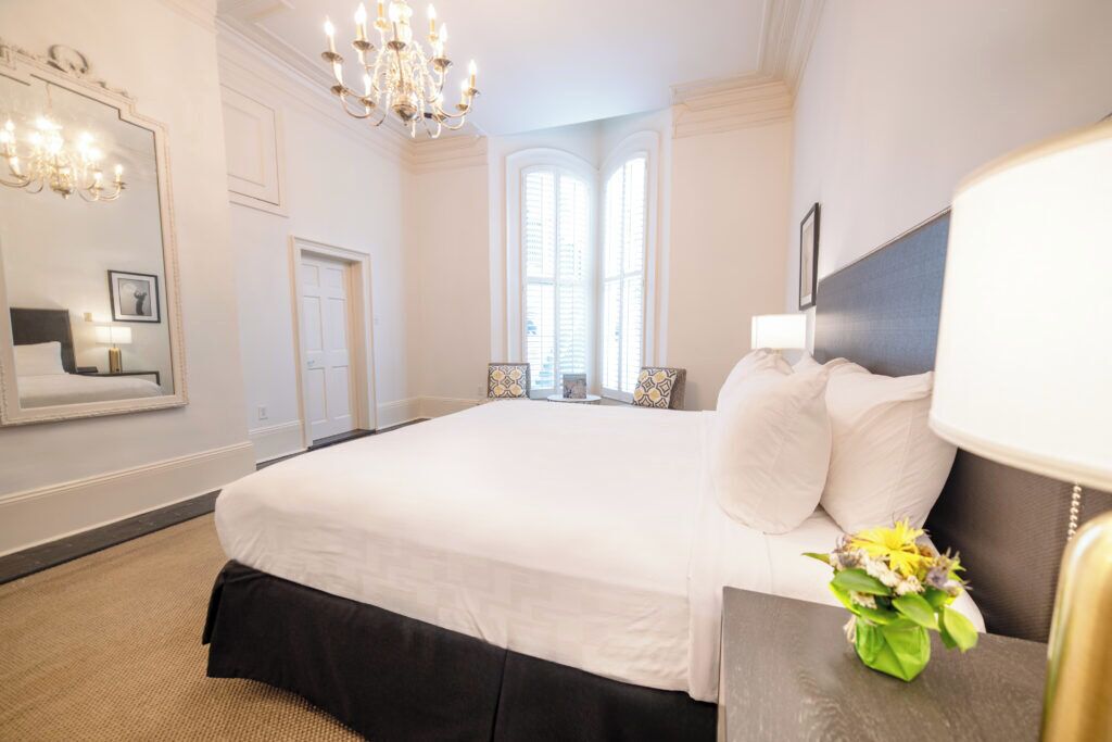 A hotel room with a large bed, a chandelier, a mirror, and a window with a view.