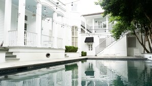 A pool area with white buildings, a staircase, and string lights. - Melrose Mansion (New Orleans)