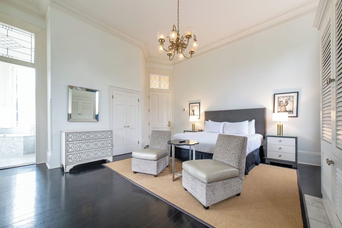 Une chambre spacieuse avec un grand lit, deux fauteuils, une petite table et un lustre.