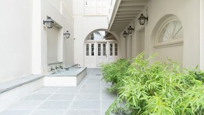 A clean, white exterior of a building with a tiled entrance, a water feature, and green plants. - Melrose Mansion (New Orleans)