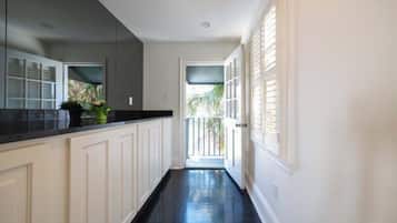 A narrow hallway with white cabinetry and a black countertop, leading to a door with a view of palm trees outside.