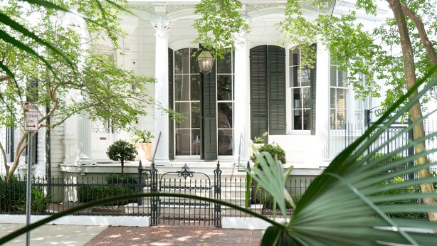A white building with green shutters, a no parking sign, and a brick pathway leading to a gated entrance. - Melrose Mansion (New Orleans)