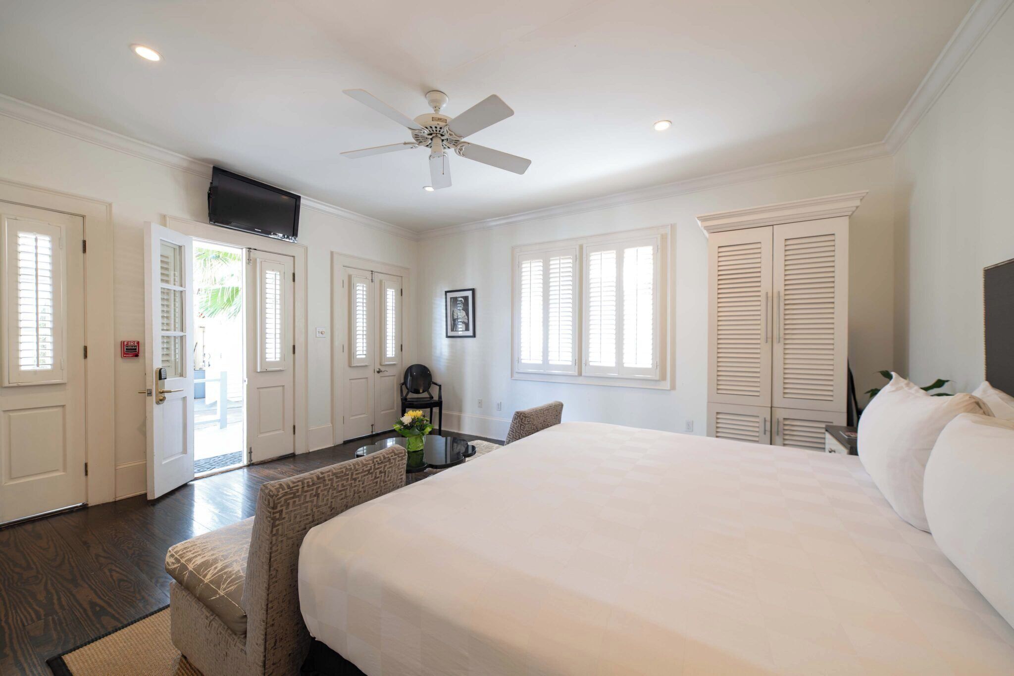 A bedroom with a large bed, a ceiling fan, and a TV mounted on the wall.