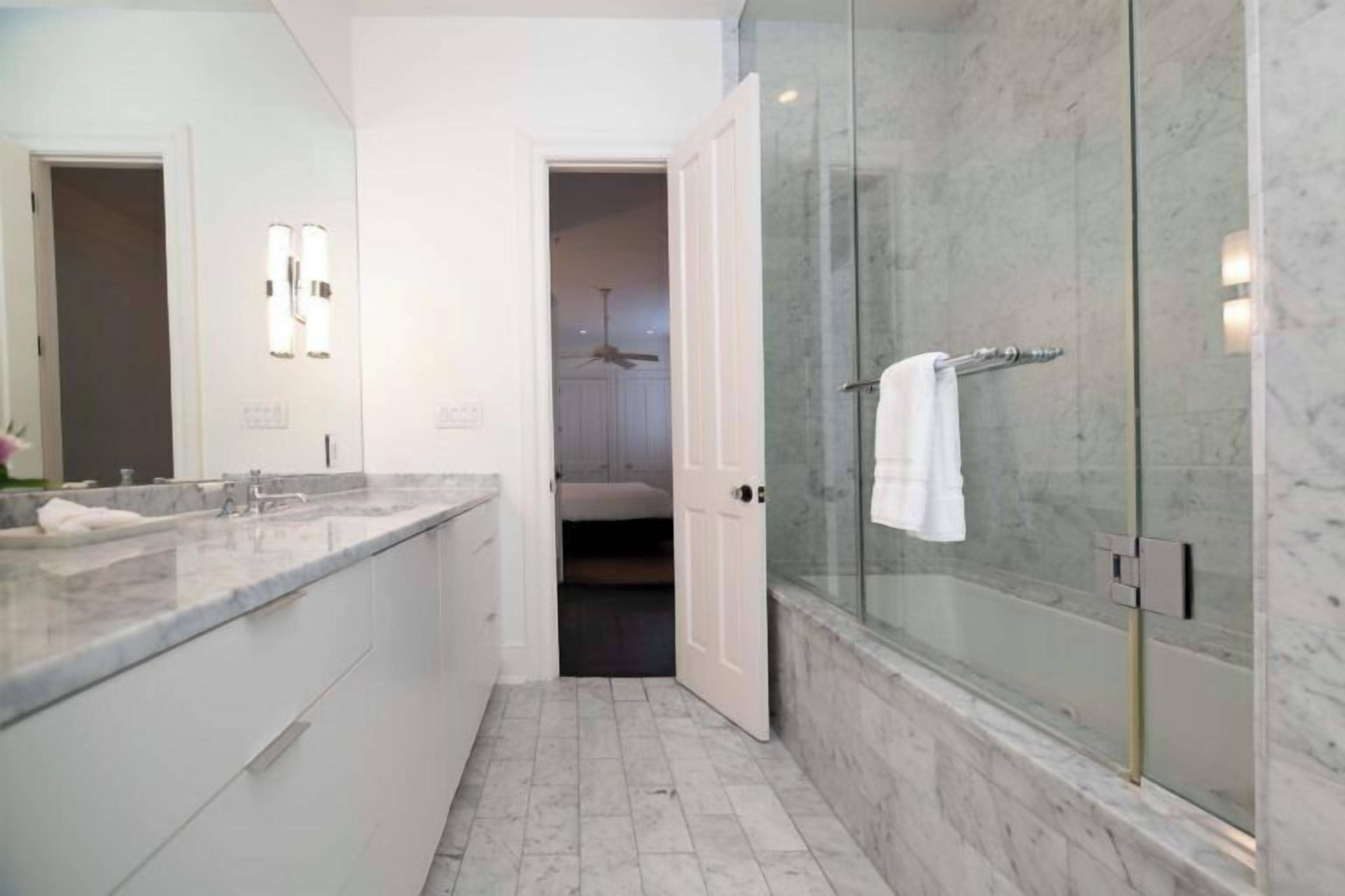 Un baño moderno con ducha de vidrio, encimera de mármol y vestidor.