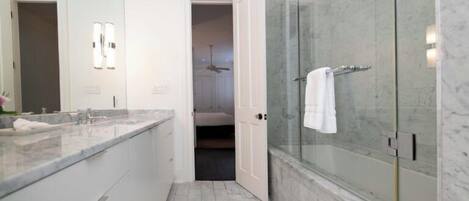 Un baño moderno con ducha de vidrio, encimera de mármol y vestidor.