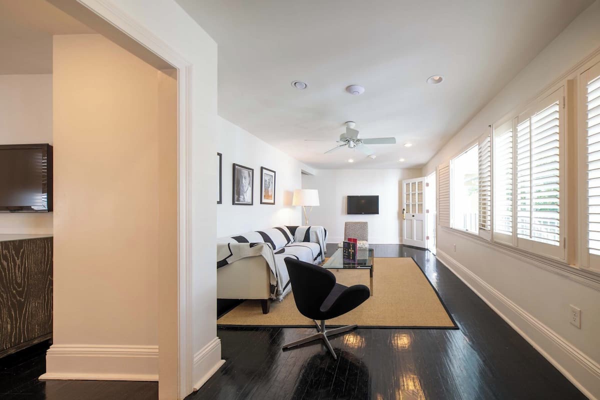 Un salon moderne avec un fauteuil noir, un canapé, un téléviseur et un ventilateur de plafond.