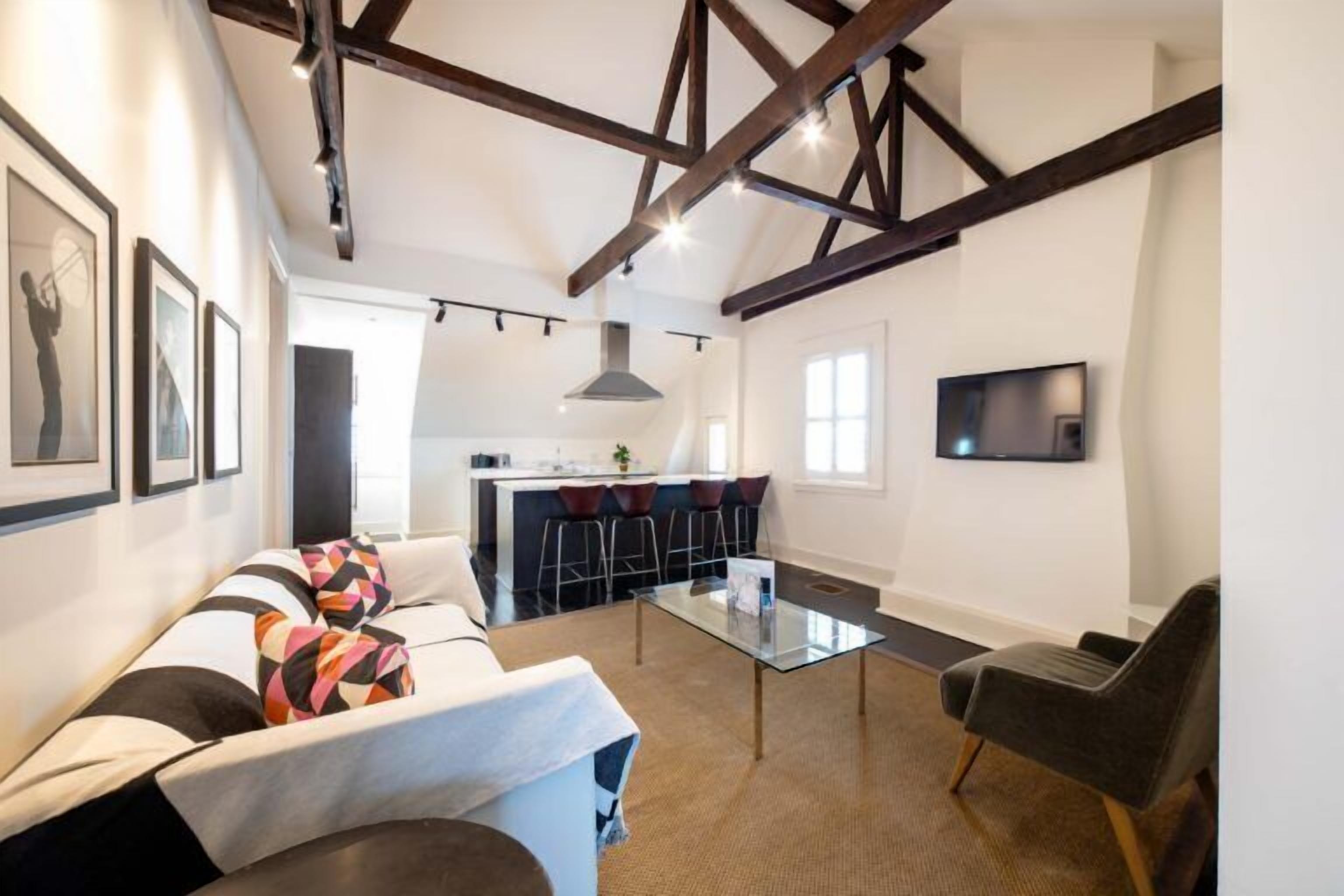 Een moderne woonkamer met een bank, een glazen salontafel en een aan de muur bevestigde televisie.
