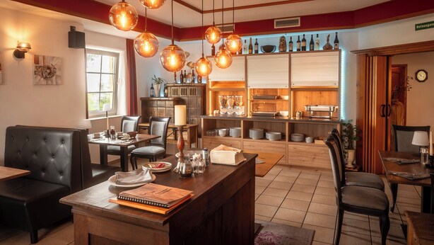 Interior de un restaurante con barra, asientos y cocina al fondo.