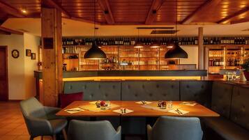 A restaurant with a wooden bar, cushioned seating, and pendant lighting.
