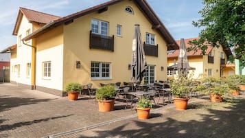 Ein gelbes Gebäude mit Außenbestuhlung und Topfpflanzen.