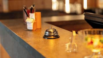 Ein Hotel-Rezeptionsbereich mit einem Holzboden, einer Klingel, einem Glasbehälter für Stifte und einem Stapel Papier.
