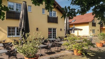 An outdoor patio area with tables and chairs, umbrellas, and potted plants.