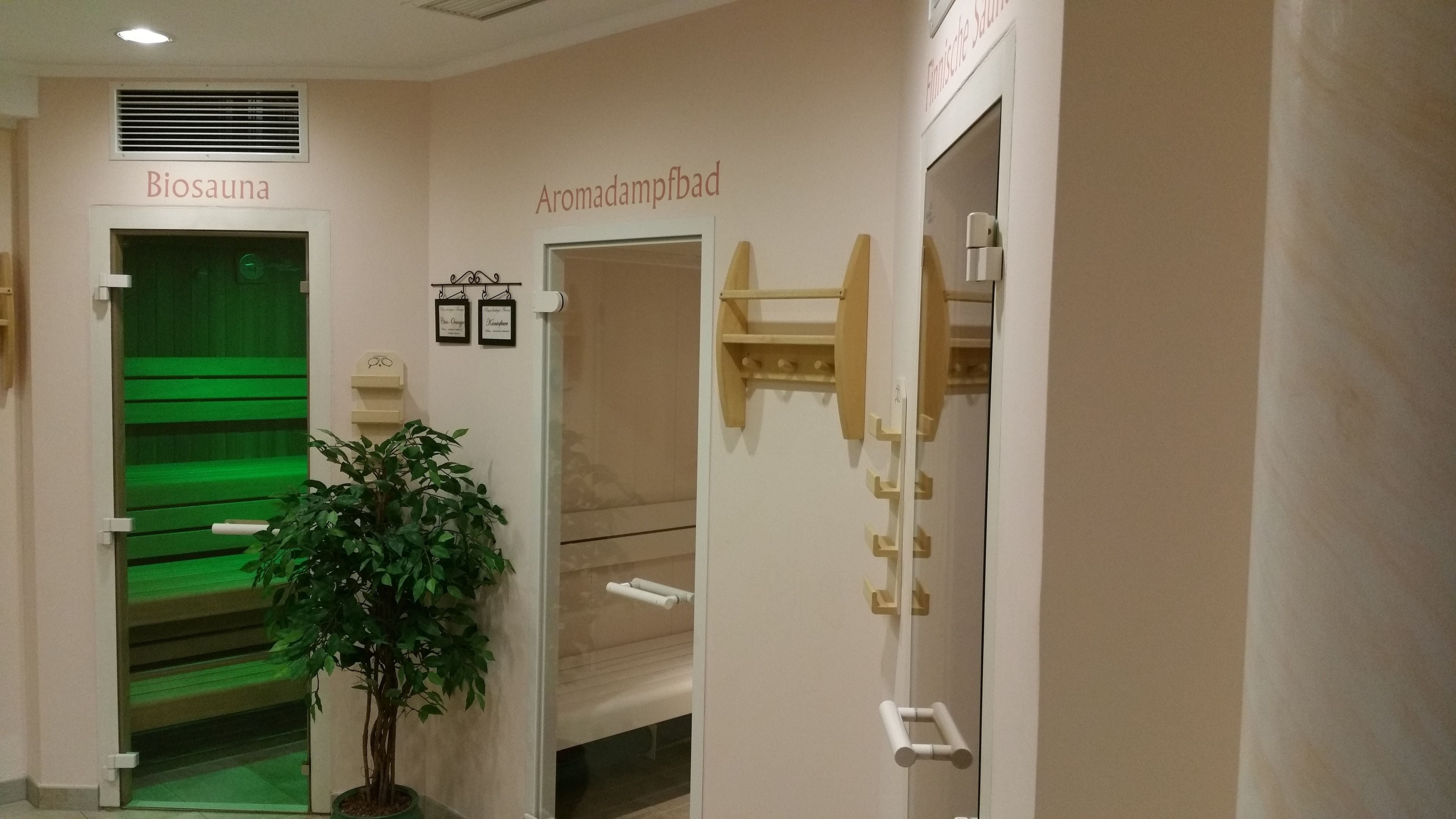 A hallway with a green bench, a potted plant, and signs for 'Biosauna' and 'Armadampfbad'.
