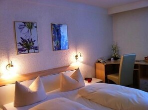Habitación de hotel con cama, dos lámparas de pared, un escritorio con silla y dos cuadros en la pared.