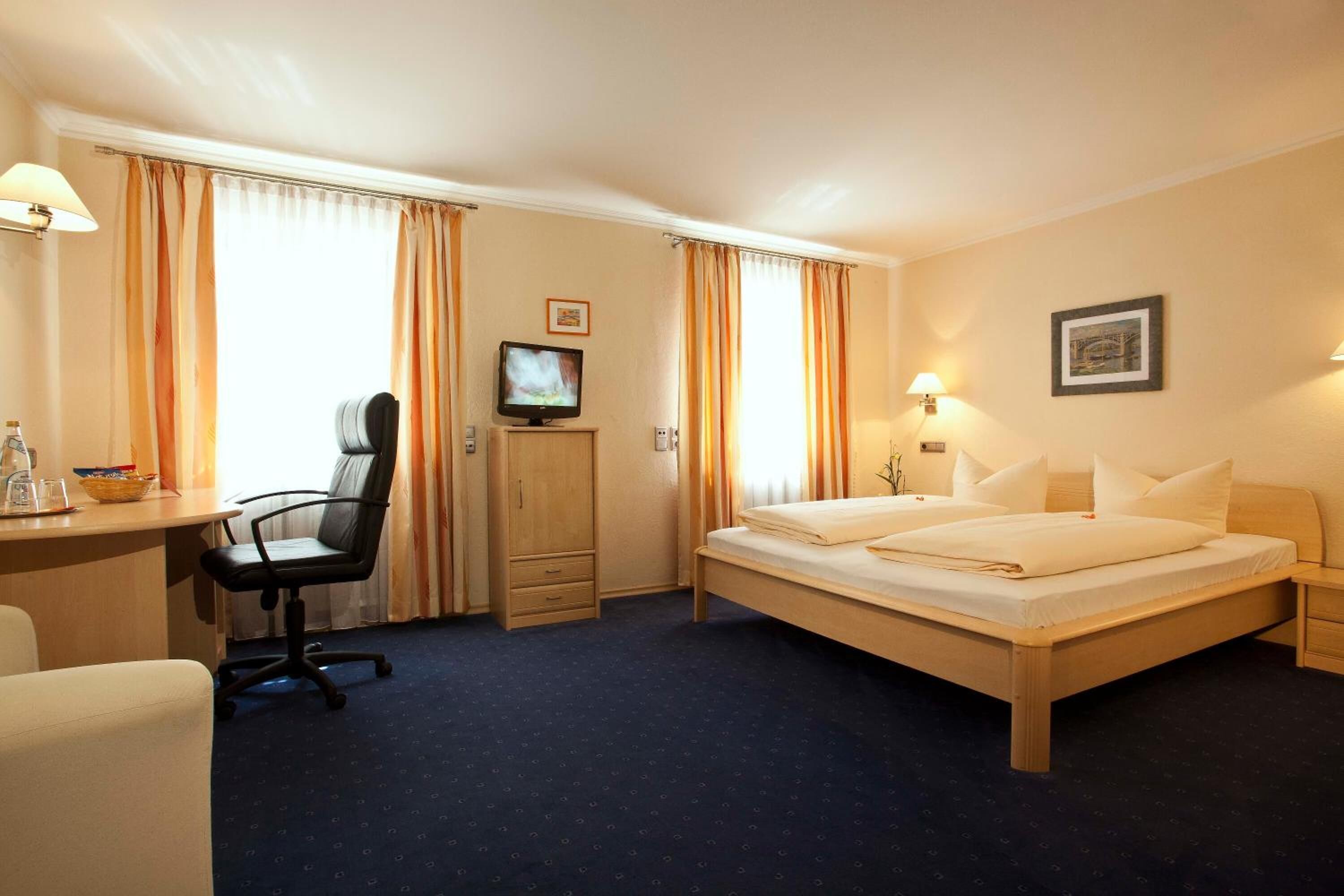 A hotel room with a bed, desk, chair, television, and curtains.