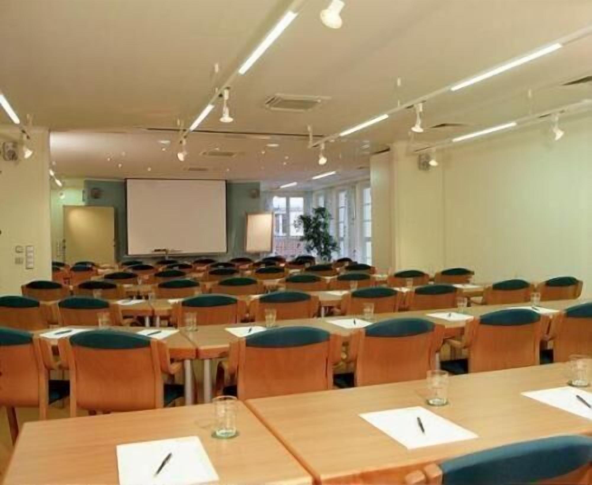 A conference room with rows of tables and chairs, a projector screen, and a large window.