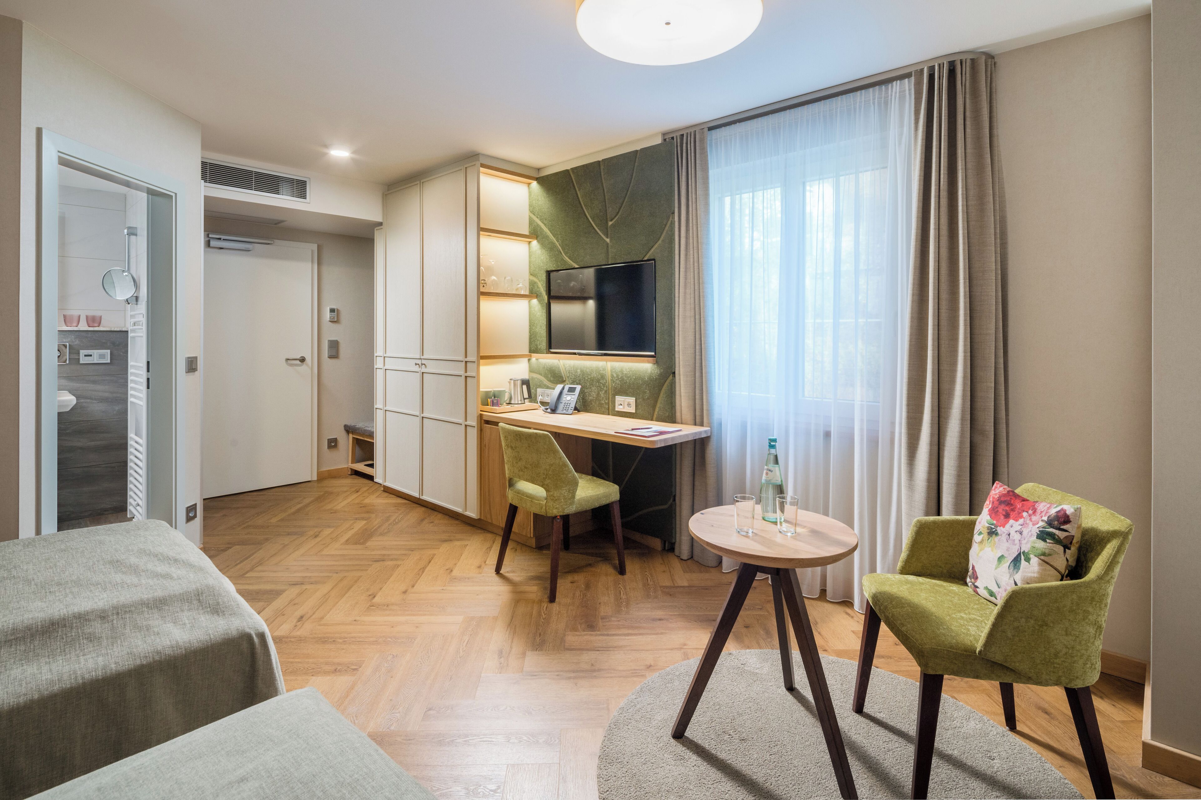 Habitación de hotel con cama, escritorio, silla, televisor y ventana con cortinas.