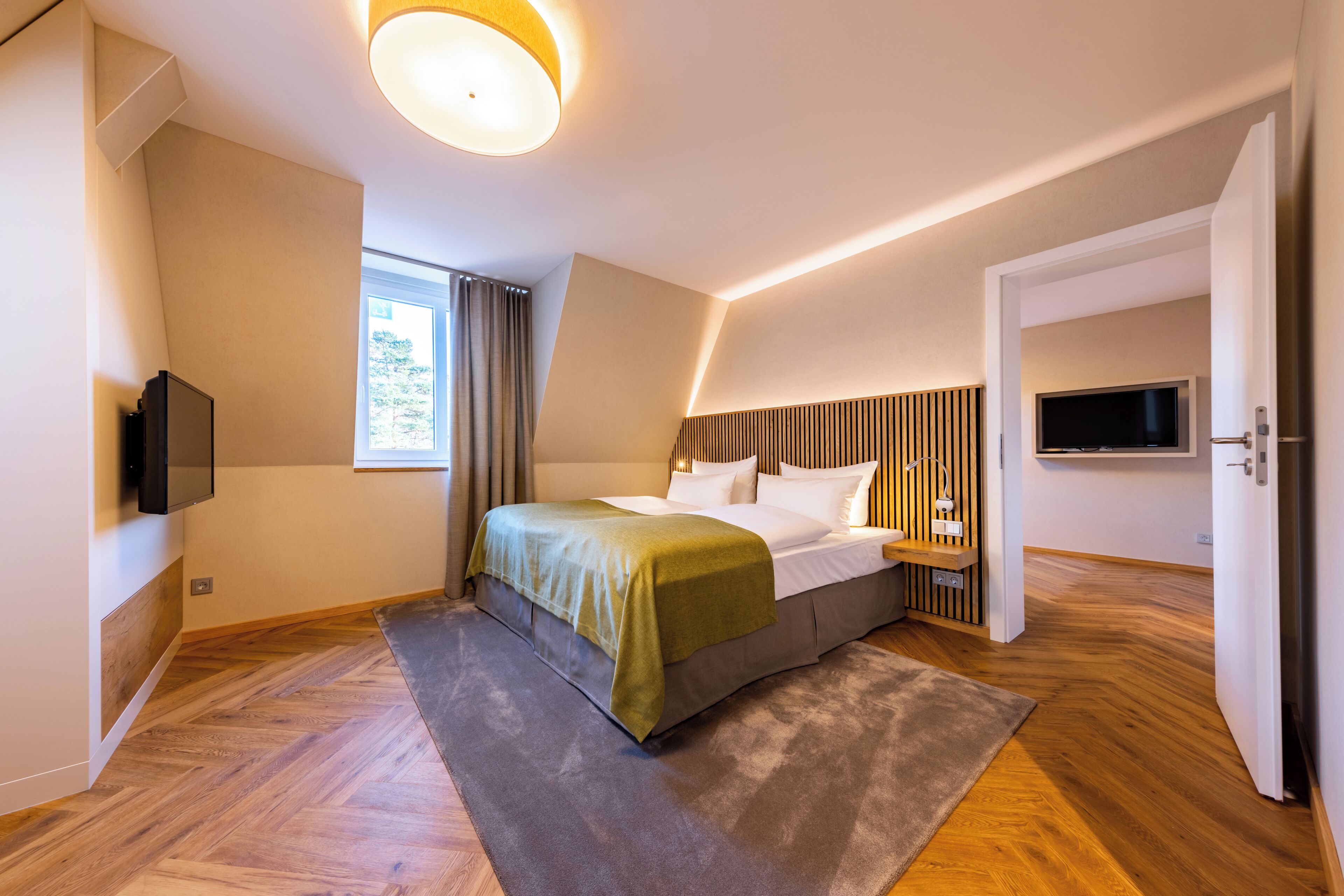 Una habitación de hotel moderna con una cama, televisor y un ventanal grande.