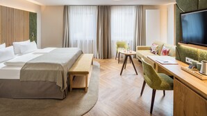 Habitación de hotel con cama, escritorio, silla, sofá, televisión y ventana con cortinas.