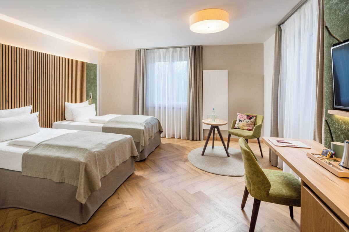 Habitación de hotel con dos camas, un escritorio, una silla, un televisor y una ventana con cortinas.