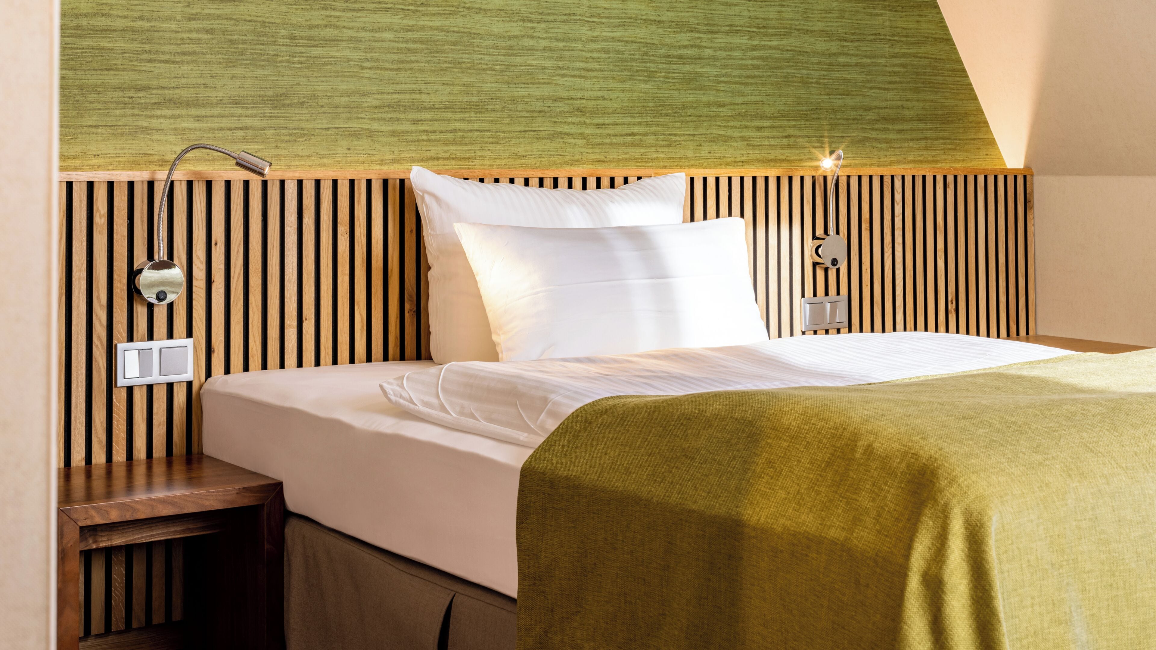 Een hotelkamer met een bed, nachtkastje, wandlamp en een lichtschakelaar.