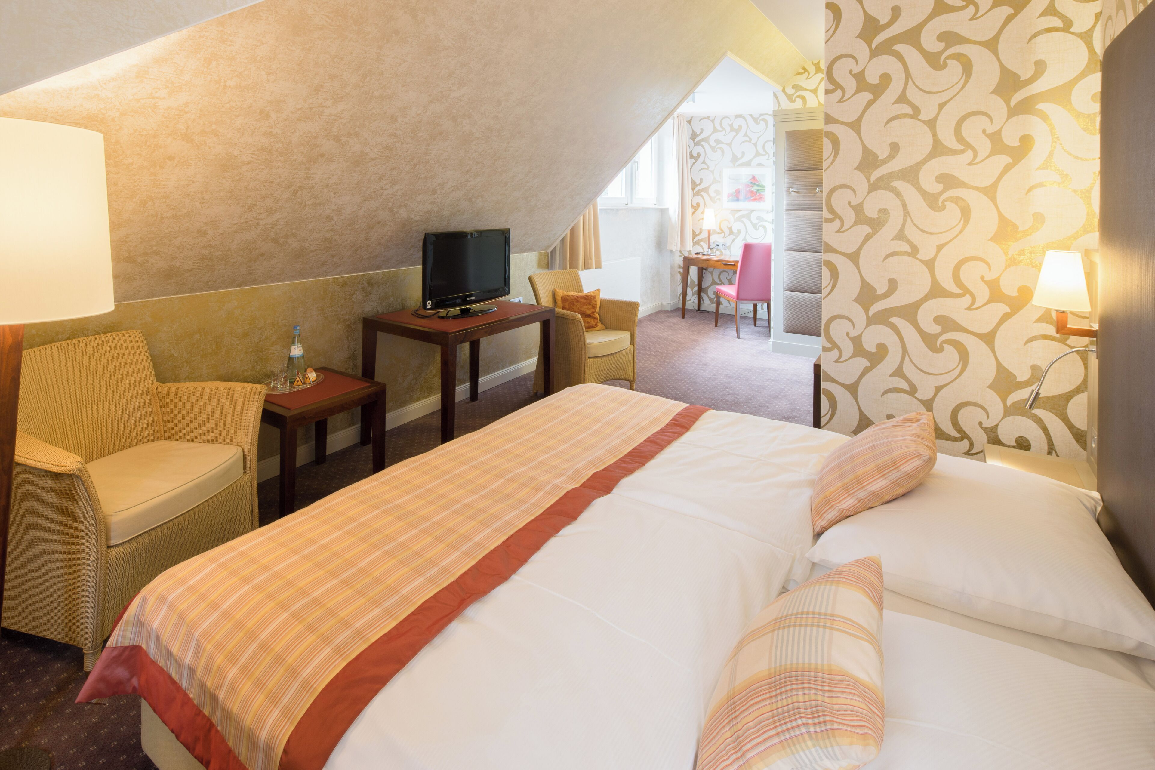 Habitación de hotel con una cama grande, televisor, escritorio y una silla.