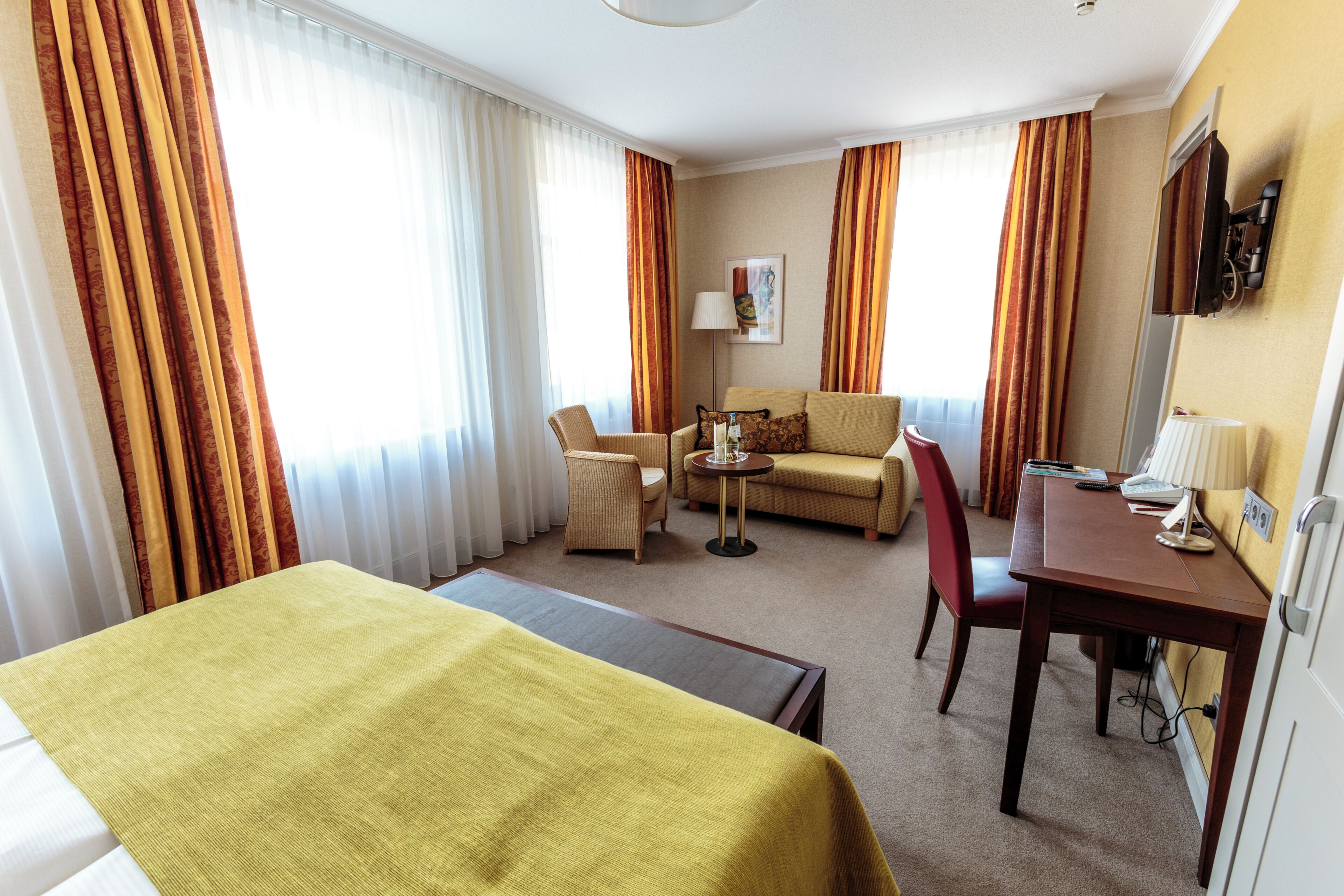 A hotel room with a bed, a sofa, a desk with a chair, and a small table.